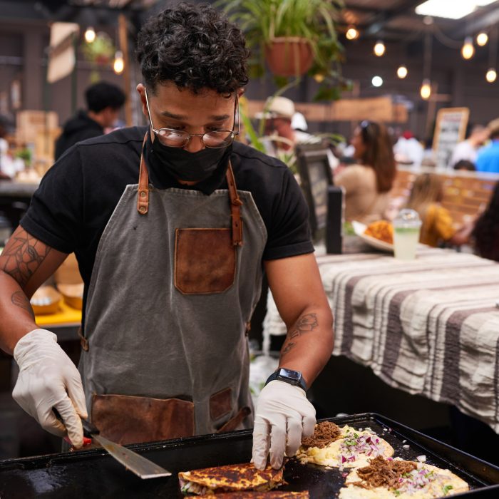 A multi-ethnic chef folds over tacos on the grill at a busy food market. High quality photo